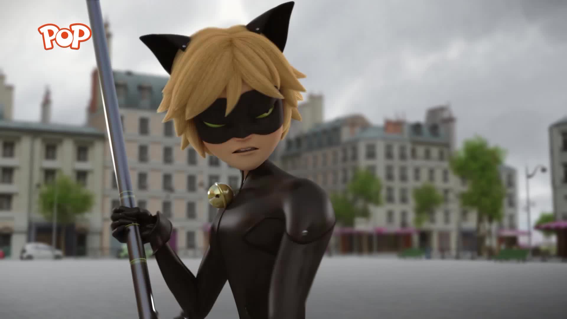 A young man in a black cat costume stands with a staff, his expression grim. Buildings with ornate facades line the square, a familiar sight in a city like Paris.