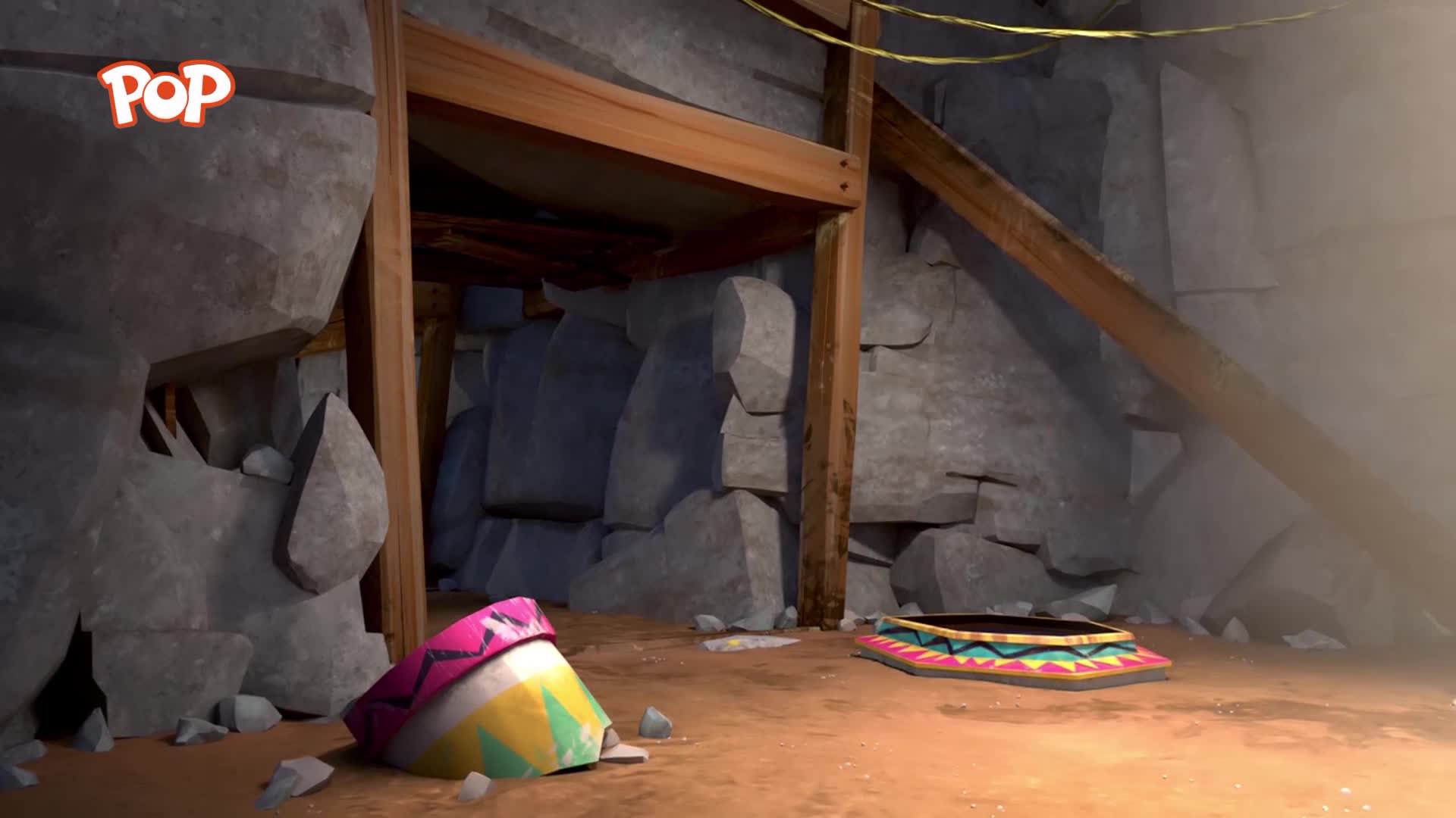 A colourful patterned mat lies on the dusty ground. Nearby, a bright, conical object rests against a rocky wall. A colourful patterned mat lies on the dusty ground. Nearby, a bright, conical object rests against a rocky wall.