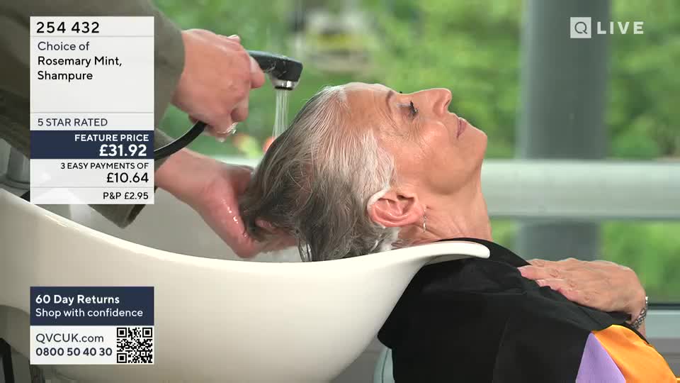 A woman reclines in a salon sink as water streams over her silver hair. The scene is part of a QVC Beauty segment, with the product details displayed on screen.
