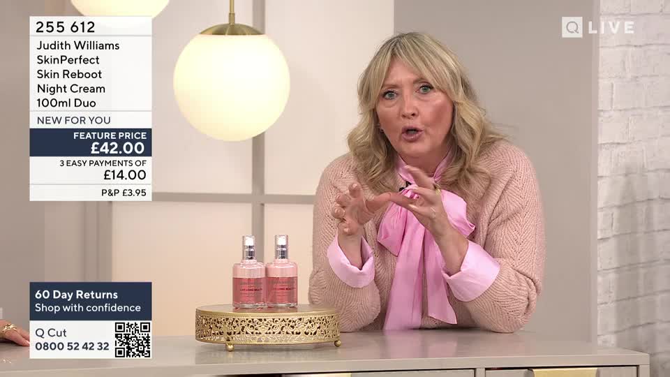 A woman in a pink sweater gestures emphatically with her hands, speaking into the camera. Two bottles of product sit on a decorative gold stand in front of her, and a price tag is displayed on the left.
