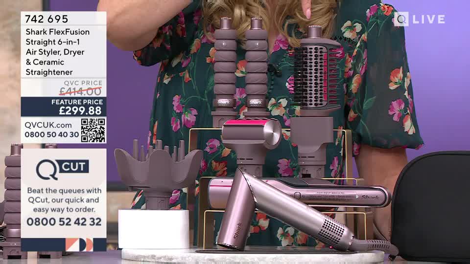 A presenter in a floral dress gestures toward a collection of hair styling tools. The Shark FlexFusion set is displayed on a stand, with its various attachments clearly visible.
