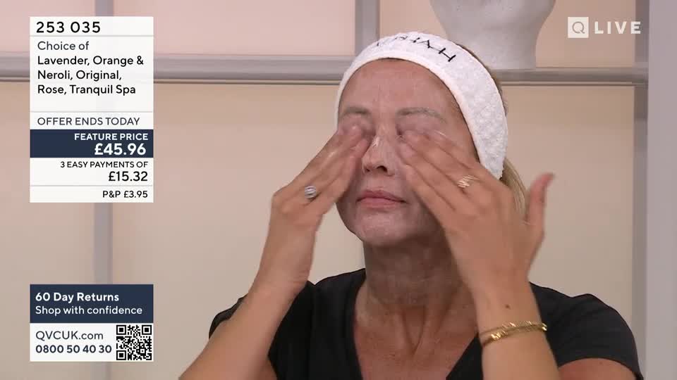 A woman, wearing a headband, gently massages a cream around her eyes. Her fingers move slowly, and her eyes are closed.

