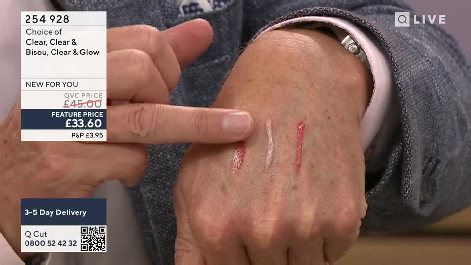 On QVC Beauty, a presenter demonstrates lip gloss shades, swiping them onto his hand. The three lines of color, from light to dark, are visible against his skin.
