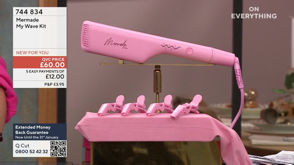 A pink curling iron, branded "Mermade," rests on a stand, with four matching clips arranged below. The item is being presented on QVC Beauty in the United Kingdom, with pricing information displayed on the left.
