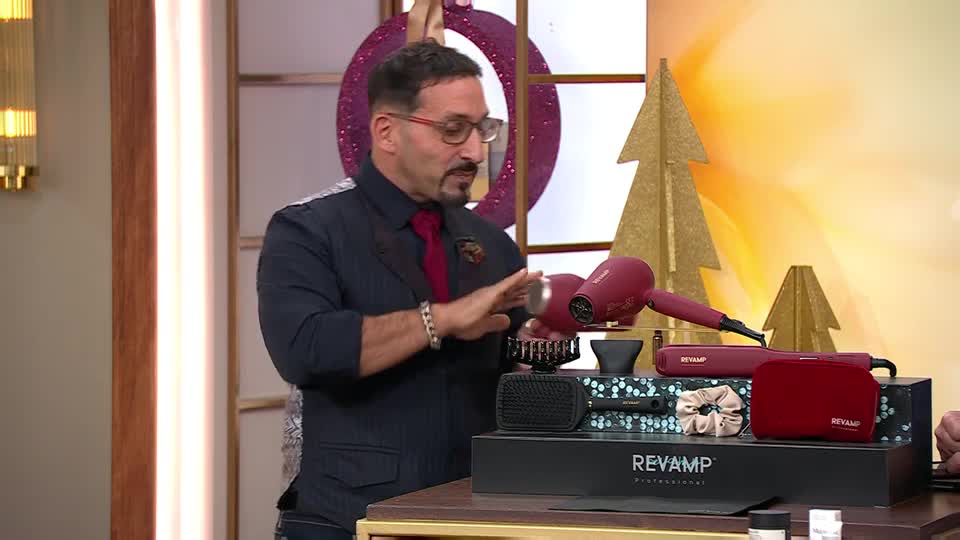 A man in a suit gestures towards a hair dryer and accessories, all neatly arranged on a table. The QVC Beauty presenter is showcasing a Revamp hair styling set, with festive decorations in the background.
A man in a suit gestures towards a hair dryer and accessories, all neatly arranged on a table. The QVC Beauty presenter is showcasing a Revamp hair styling set, with festive decorations in the background.