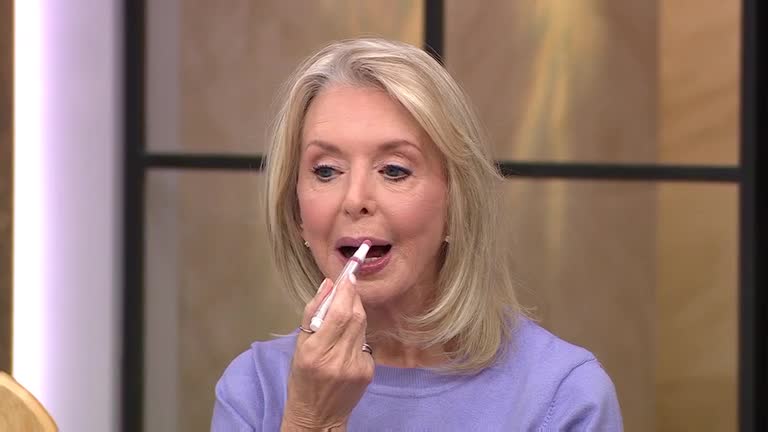 A woman with blonde hair carefully applies lipstick with a white applicator, her expression focused. She's on a QVC Beauty segment, demonstrating a product for the UK audience.
A woman with blonde hair carefully applies lipstick with a white applicator, her expression focused. She's on a QVC Beauty segment, demonstrating a product for the UK audience.
