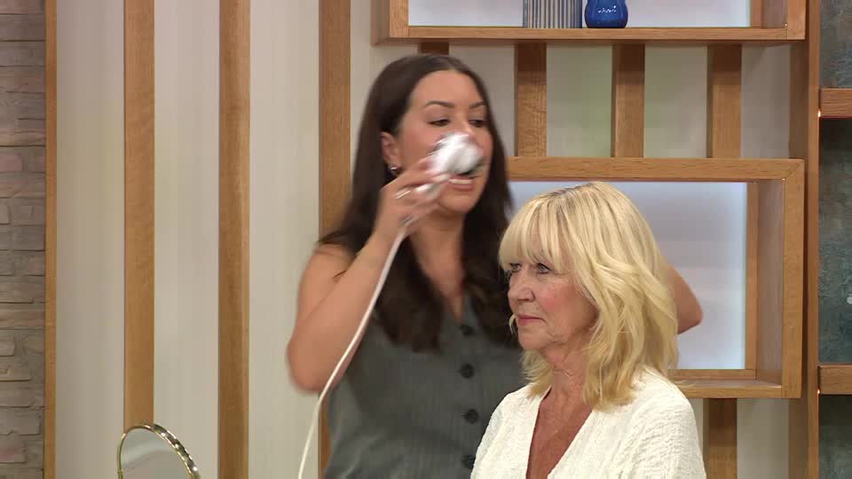 A woman in a grey top holds a white device up to another woman's face, demonstrating its use. The blonde-haired woman looks on, as if waiting for the demonstration to begin.
A woman in a grey top holds a white device up to another woman's face, demonstrating its use. The blonde-haired woman looks on, as if waiting for the demonstration to begin.