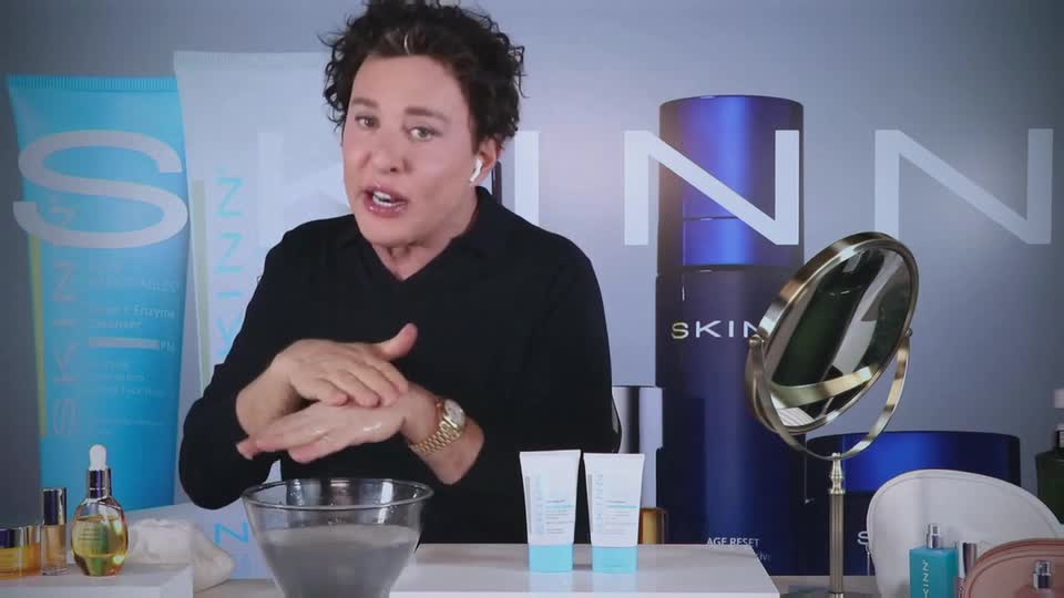 A man in a black shirt is demonstrating a skincare product, rubbing it into his hands. Behind him, the backdrop features large product packaging and the word "SKINN."
A man in a black shirt is demonstrating a skincare product, rubbing it into his hands. Behind him, the backdrop features large product packaging and the word "SKINN."