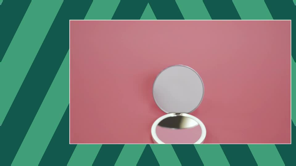 A compact mirror, open, sits on a pink surface. The reflection in the lower mirror shows a hint of blush.
