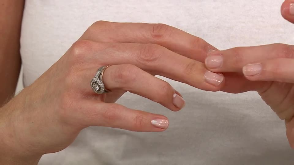 A hand, adorned with a sparkling ring, gently touches another, showing off the freshly manicured nails. The focus is on the close-up of the hands, highlighting the natural nail color.
