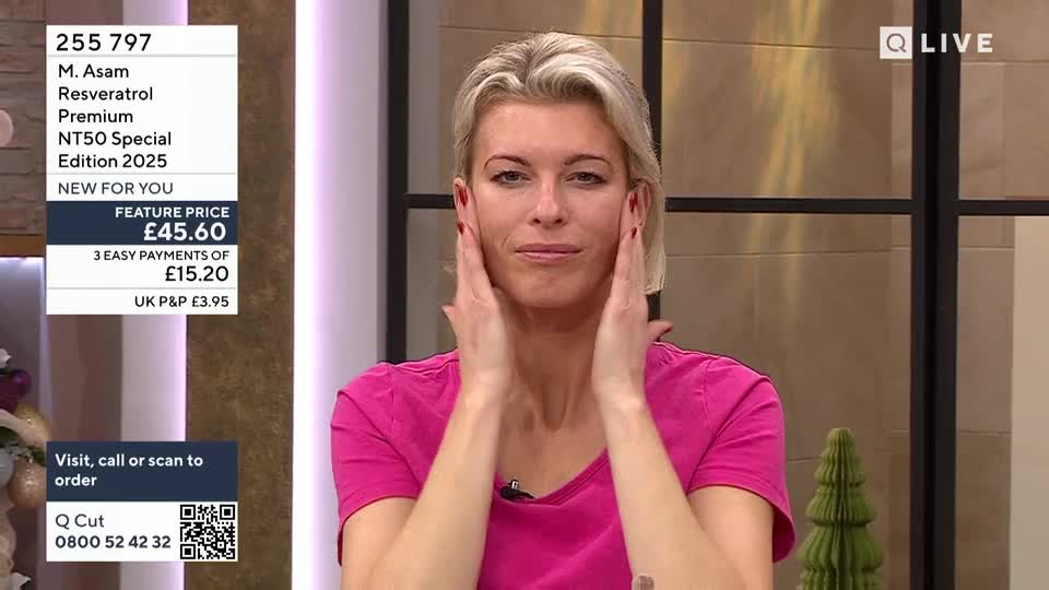 A woman on QVC Beauty in the United Kingdom gently presses her hands against her cheeks. She's demonstrating a skincare product, likely the M. Asam Resveratrol Premium NT50 Special Edition.
