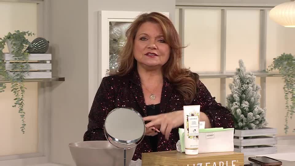 The woman in the sequined jacket gestures towards a selection of beauty products. A small mirror and a washbowl sit in front of her, ready for the demonstration.
