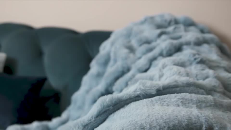 A plush, pale blue throw is draped over a dark teal sofa. The fabric has a soft, textured pile that catches the light.