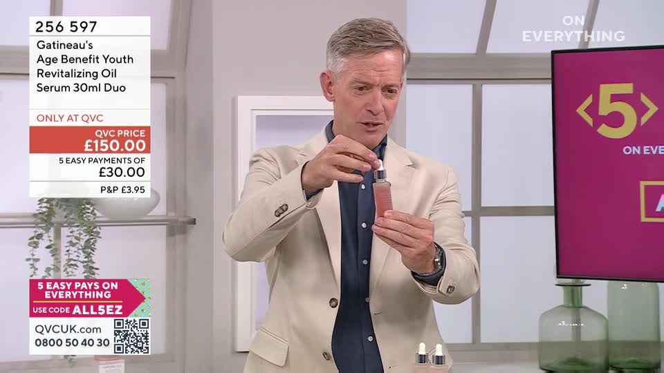 A man in a light jacket holds up a small glass bottle of pink serum, demonstrating its application. On the screen behind him, a large "5" is displayed, indicating a special offer for QVC viewers.