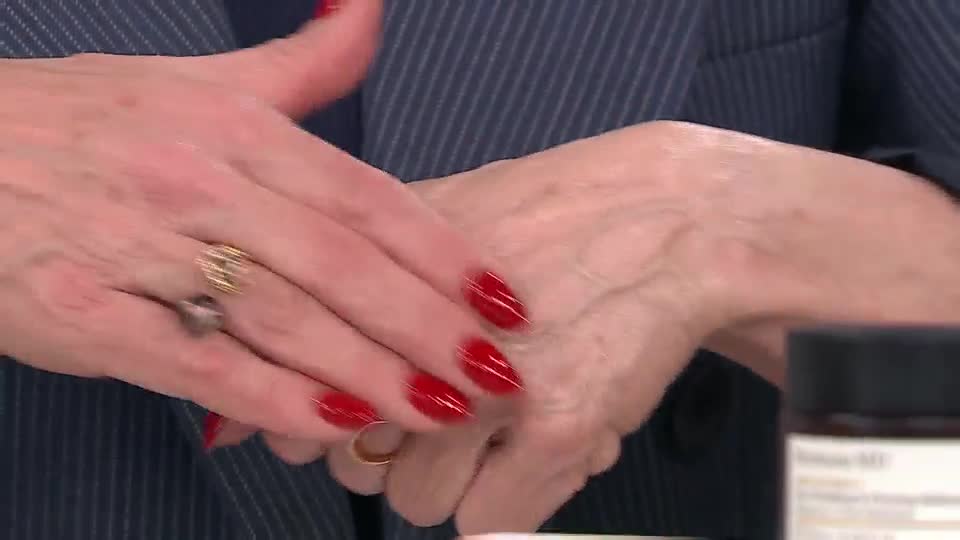 The presenter is demonstrating a beauty product, rubbing cream into her hands. Her bright red nails stand out against her skin as she works the product in.