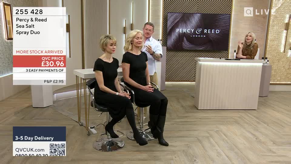 A man gestures towards two women seated on stools, demonstrating a hair product. A screen behind them displays the Percy & Reed London logo.