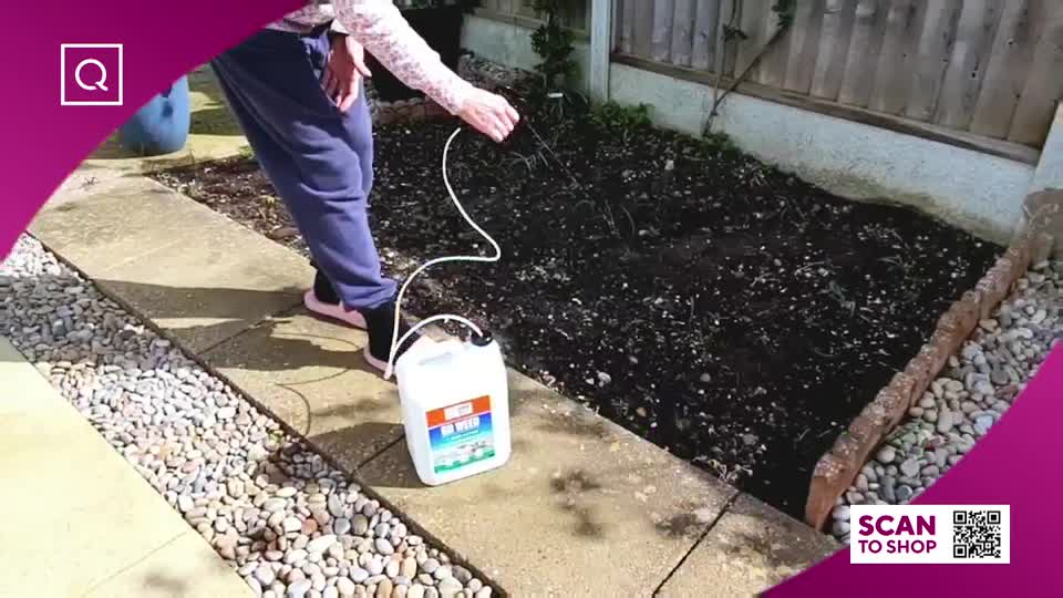 A person is spraying a garden bed with a hose connected to a white plastic container. The container has a label that reads "Weed Killer."