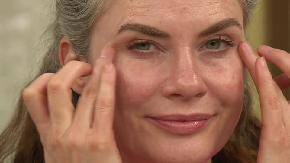 Fingertips gently pat a cream around the eyes. A woman smiles, her makeup looking fresh for her QVC Beauty segment.