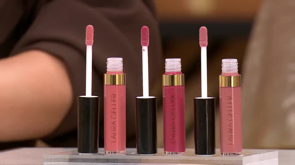 Five Laura Geller lip glosses stand in a row, their applicators extended. The QVC Beauty presenter's arm is visible behind them.