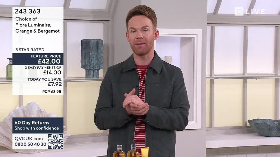 A man in a dark jacket and striped t-shirt stands with his hands clasped, speaking directly to the camera. On the left, a graphic displays details for a "Flora Luminaire, Orange & Bergamot" product, including its price and payment options.