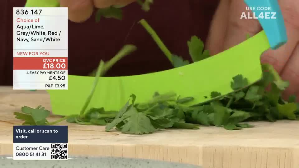 A bright green chopper is slicing through a pile of fresh parsley on a wooden board. Bits of the herb are flying up into the air as the demonstration continues on QVC Extra.
