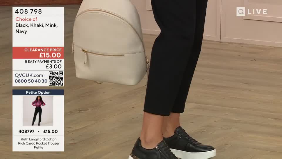 A cream-colored backpack hangs from a woman's arm, and she's wearing black trousers and platform sneakers. The QVC Extra screen shows the price and product details, all from the United Kingdom.
