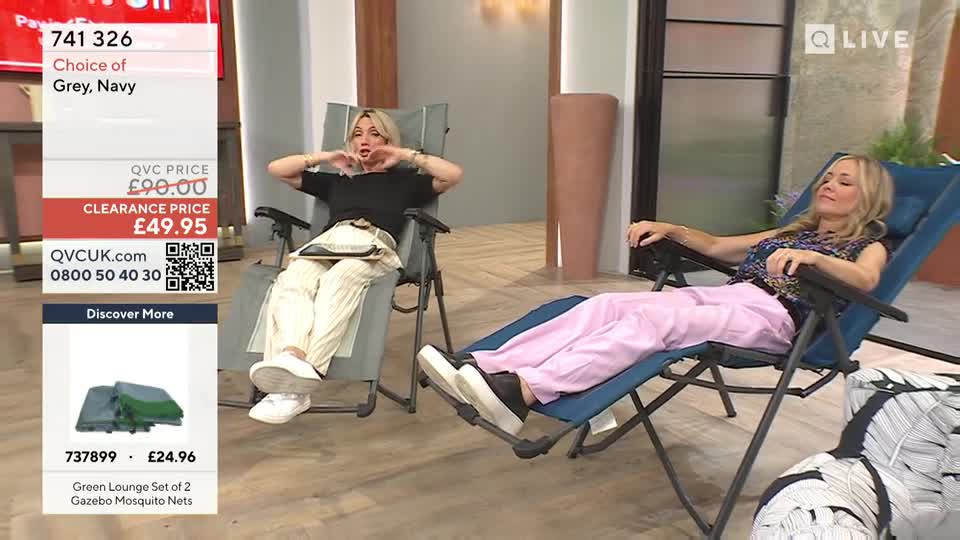 On QVC Extra, a woman in a black top gestures with her hands while seated in a reclined chair. Another woman, wearing pink pants, is relaxed in a similar chair.
