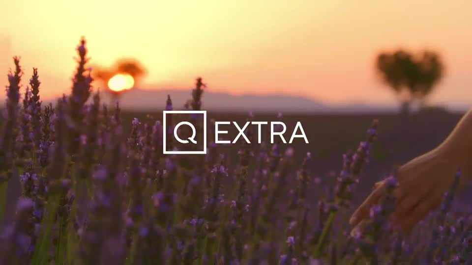 The setting sun casts a warm glow over a field of lavender. A hand gently brushes the purple flowers, as the QVC Extra logo appears.
