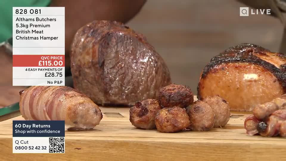 A large, cooked joint of meat sits alongside a pile of browned meatballs and a sausage wrapped in bacon, all presented on a wooden board. The QVC Extra logo is visible, and the price of a Christmas hamper is displayed on screen.
