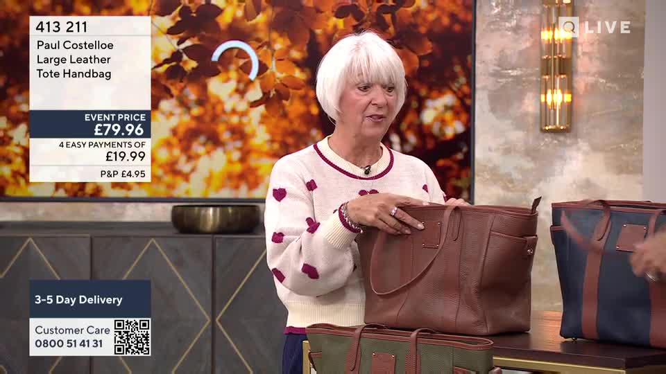 A woman in a heart-patterned sweater holds a brown leather tote bag, gesturing to its interior. Several other bags of different colors sit below, all awaiting their moment on the QVC Extra show.

