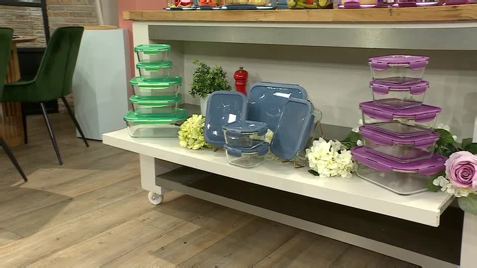 A table displays sets of food storage containers, each with different colored lids. The products are arranged alongside floral decorations, likely for a segment on QVC Extra in the United Kingdom.
