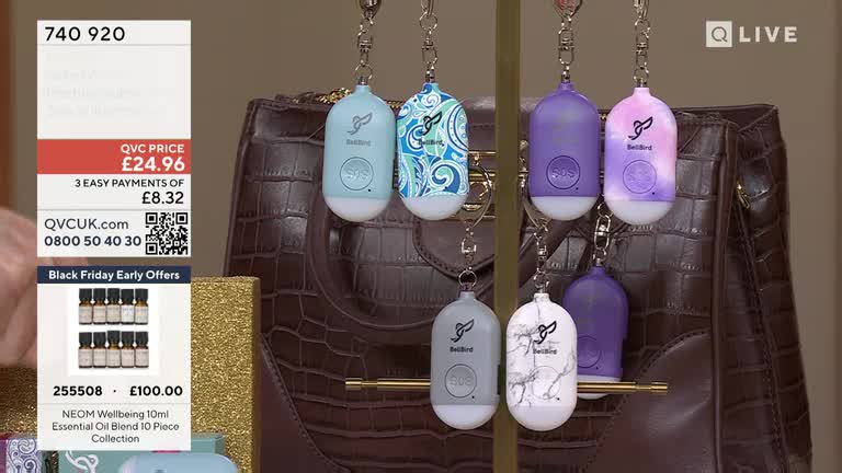 A display of colorful keychains hangs in front of a brown leather bag. The QVC Extra price of £24.96 is visible on the screen.
