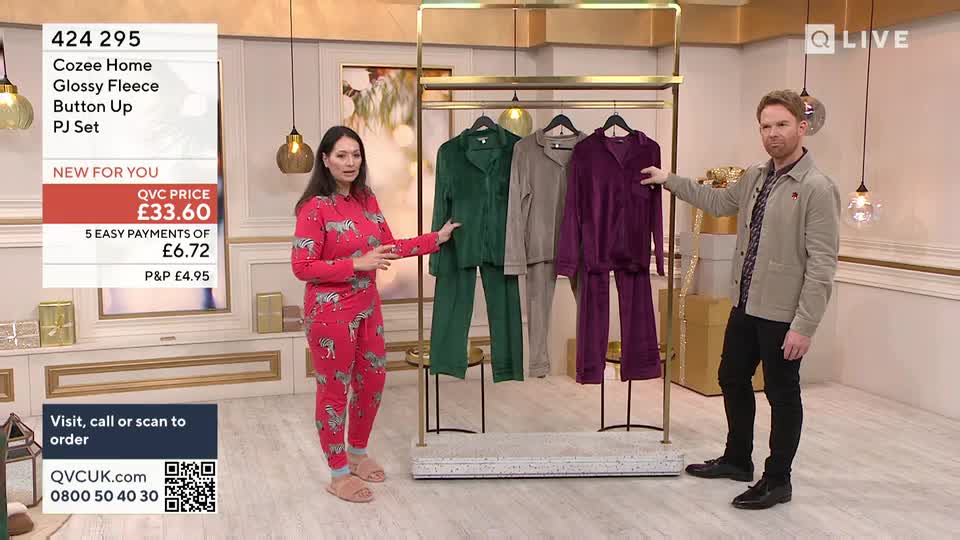 A woman in zebra-print pajamas gestures toward a rack of fleece sleepwear, while a man in a jacket points to the purple set. The QVC Extra studio is brightly lit, and the price is displayed on a screen.
