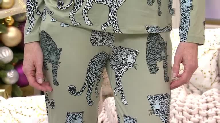 A person in a matching leopard-print outfit stands facing the camera. The light green fabric is covered with black and white spotted cats, and the presenter's hands are visible.
