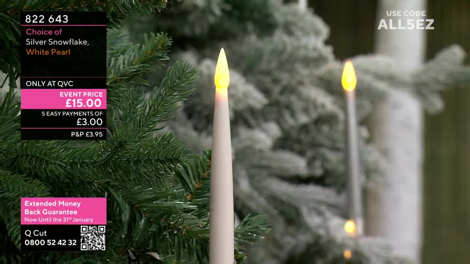 Two slender, white candles with flickering yellow flames stand out against a backdrop of a frosted Christmas tree, all presented on QVC Extra. The on-screen graphics highlight the product details and a special offer for UK viewers.
