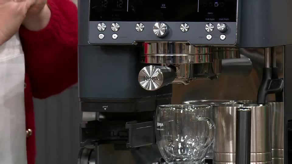A gleaming espresso machine sits on a counter, ready to brew. Two clear glass mugs are positioned below the spout, awaiting their fill.
