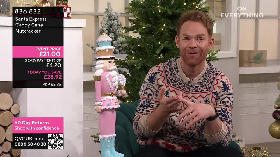A man in a Christmas sweater gestures enthusiastically, talking about a pink nutcracker standing beside him. The QVC Extra set features a decorated tree and a display of the product's price.

