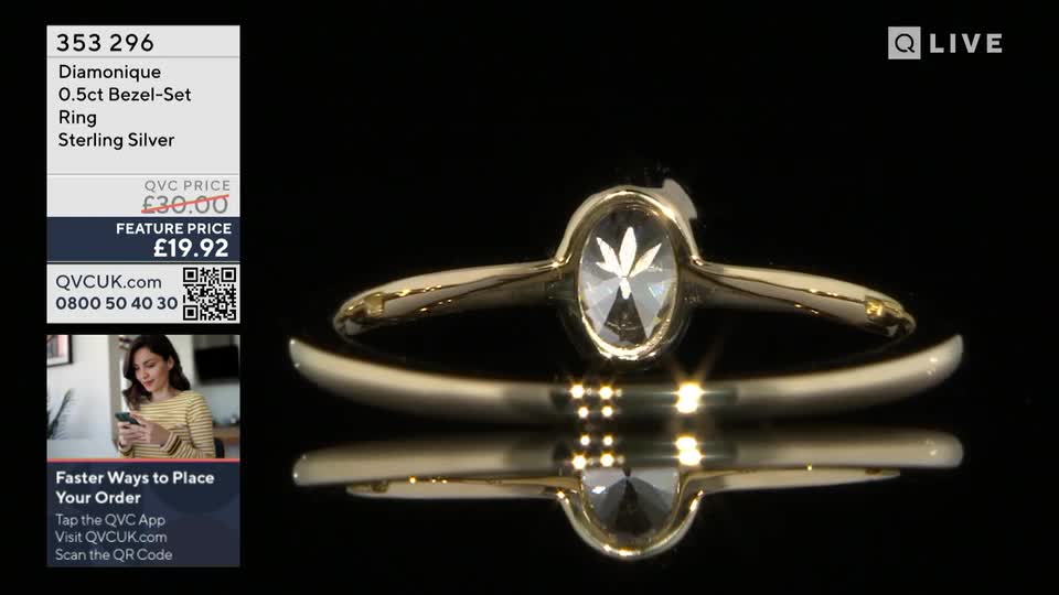 A gold ring with a clear, oval-cut stone sits on a reflective surface. On the left, a woman is shown holding a phone, with text overlaying the image detailing product information and ordering instructions for QVC UK.