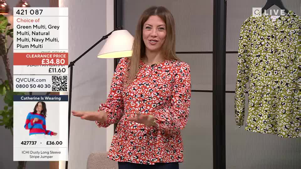 A woman in a red patterned blouse gestures animatedly, a QVC Extra graphic to her left detailing a clearance price of £34.80. To her right, a green patterned garment hangs on display. A woman in a red patterned blouse gestures animatedly, a QVC Extra graphic to her left detailing a clearance price of £34.80. To her right, a green patterned garment hangs on display.