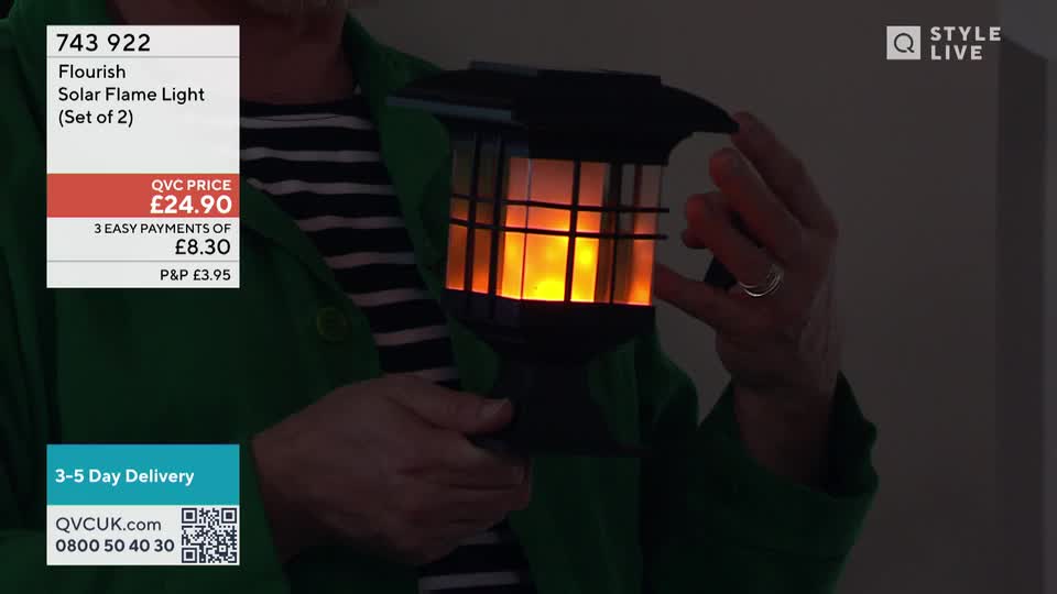 A hand holds up a black lantern with a flickering orange glow inside. The QVC Extra graphic shows the price is £24.90. A hand holds up a black lantern with a flickering orange glow inside. The QVC Extra graphic shows the price is £24.90.