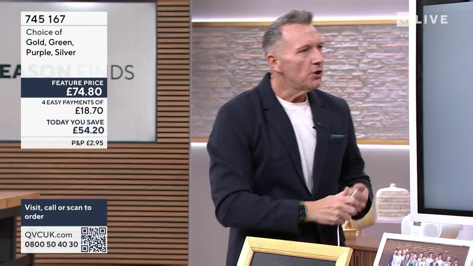 A man in a dark jacket gestures as he speaks on QVC Extra. A graphic displays a feature price of £74.80, with options for gold, green, purple, and silver. A man in a dark jacket gestures as he speaks on QVC Extra. A graphic displays a feature price of £74.80, with options for gold, green, purple, and silver.