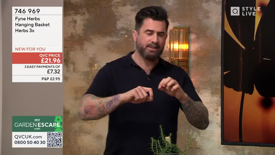 A man with tattoos on his arms gestures with his hands, holding something small between his fingers. He's on QVC Extra, discussing a hanging herb basket. A man with tattoos on his arms gestures with his hands, holding something small between his fingers. He's on QVC Extra, discussing a hanging herb basket.