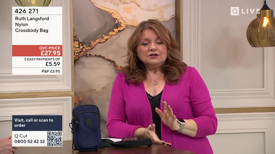 A woman in a bright pink cardigan gestures with her hands as she speaks. Beside her, a navy crossbody bag sits on a table. A woman in a bright pink cardigan gestures with her hands as she speaks. Beside her, a navy crossbody bag sits on a table.