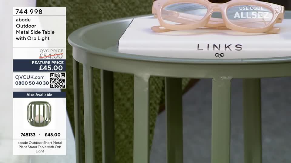 A pale pink pair of glasses rests on a white book with "LINKS" printed on it. The book sits atop a sage green metal side table.