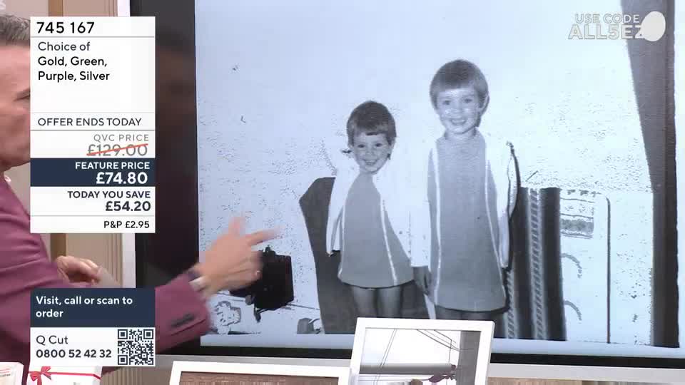A man in a suit points at a black and white photograph of two smiling children. On the left, a screen displays product details and pricing for QVC Extra.