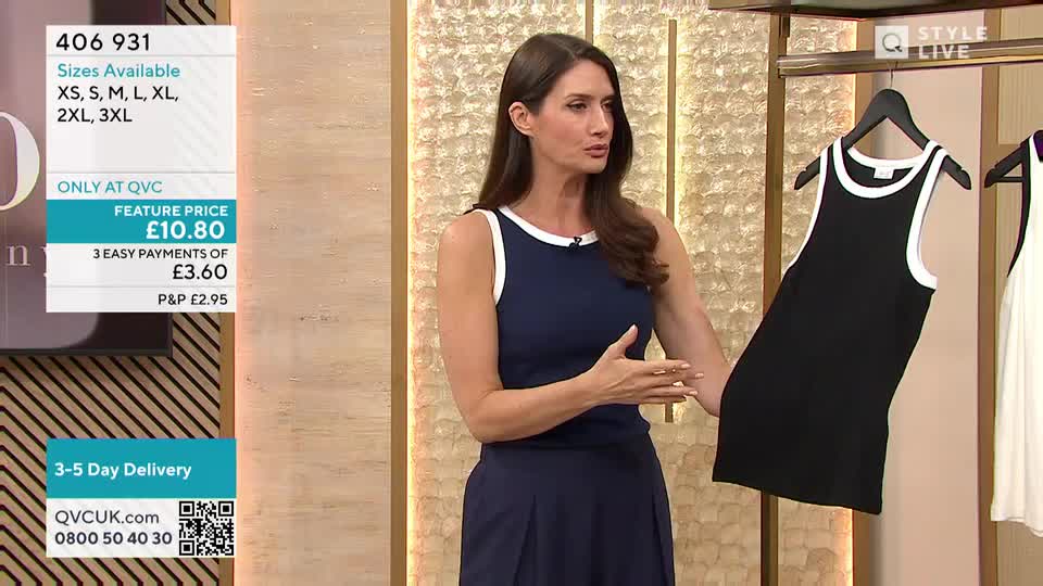 A woman in a blue dress gestures towards a black tank top with white trim, held up on a hanger. The screen displays the item's price and size options, all presented in a QVC UK style.
