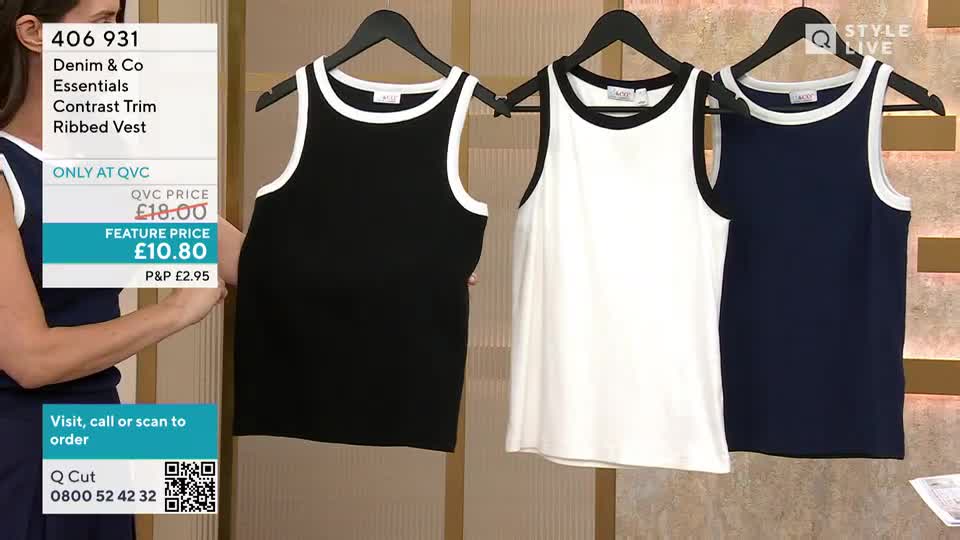 A woman in a navy top holds a black vest with a white trim, showing it off for the QVC audience. Three vests hang on black hangers: black, white, and navy, each with a contrasting trim.
