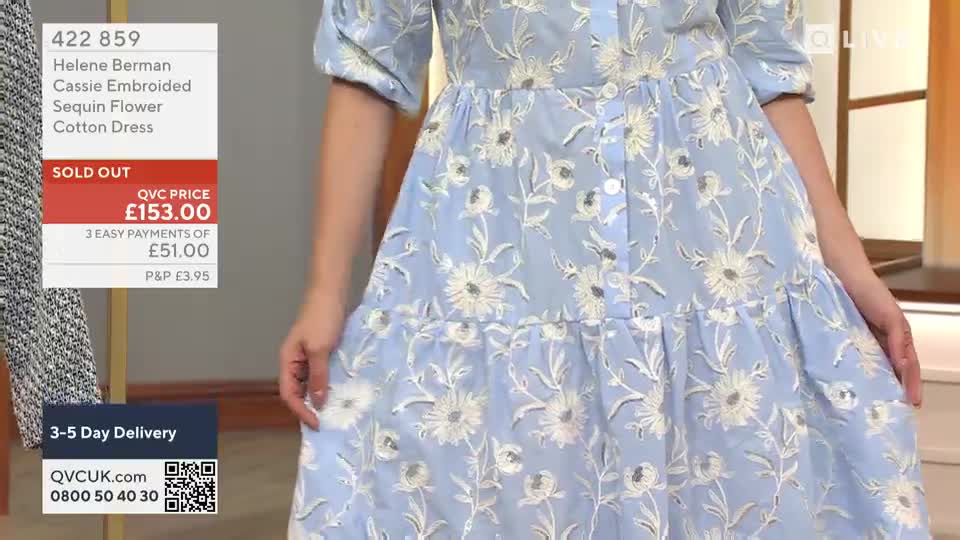 A woman in a light blue dress with white floral embroidery is holding the fabric out, showing off the design. The QVC price is displayed on the screen, and it's already sold out.
