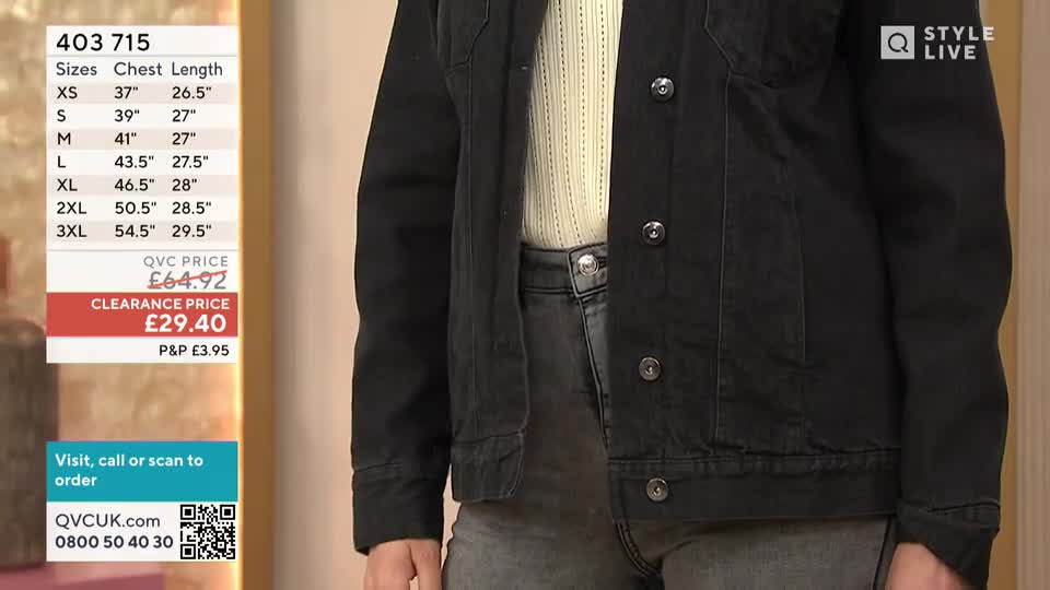 A model, clad in a black denim jacket over a cream sweater, stands still, showing off the garment's fit. The QVC price and size chart are displayed on a screen beside them.
