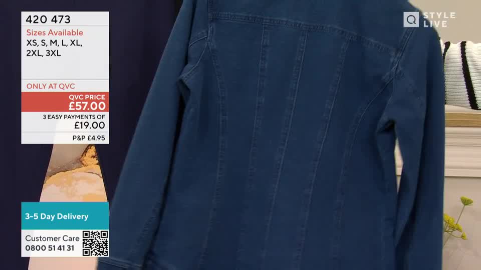 A denim jacket, shown from the back, is being held up on a QVC Style Live set. The camera focuses on the jacket's details, with a price tag and size information displayed on the screen.

